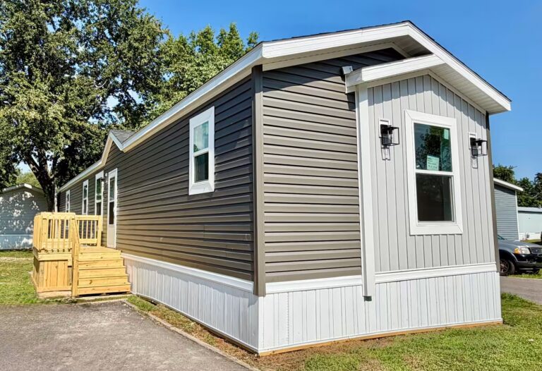 Gray manufactured home with white trim and wooden deck stairs under blue sky