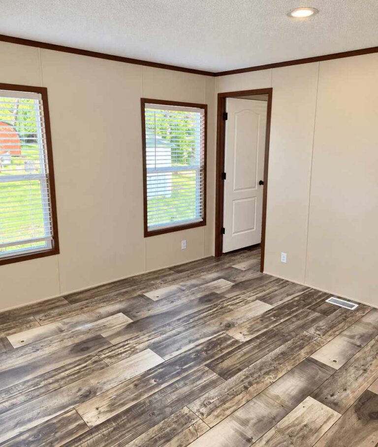 Empty room with wood-look flooring, beige walls, two windows with blinds, and an open white door.