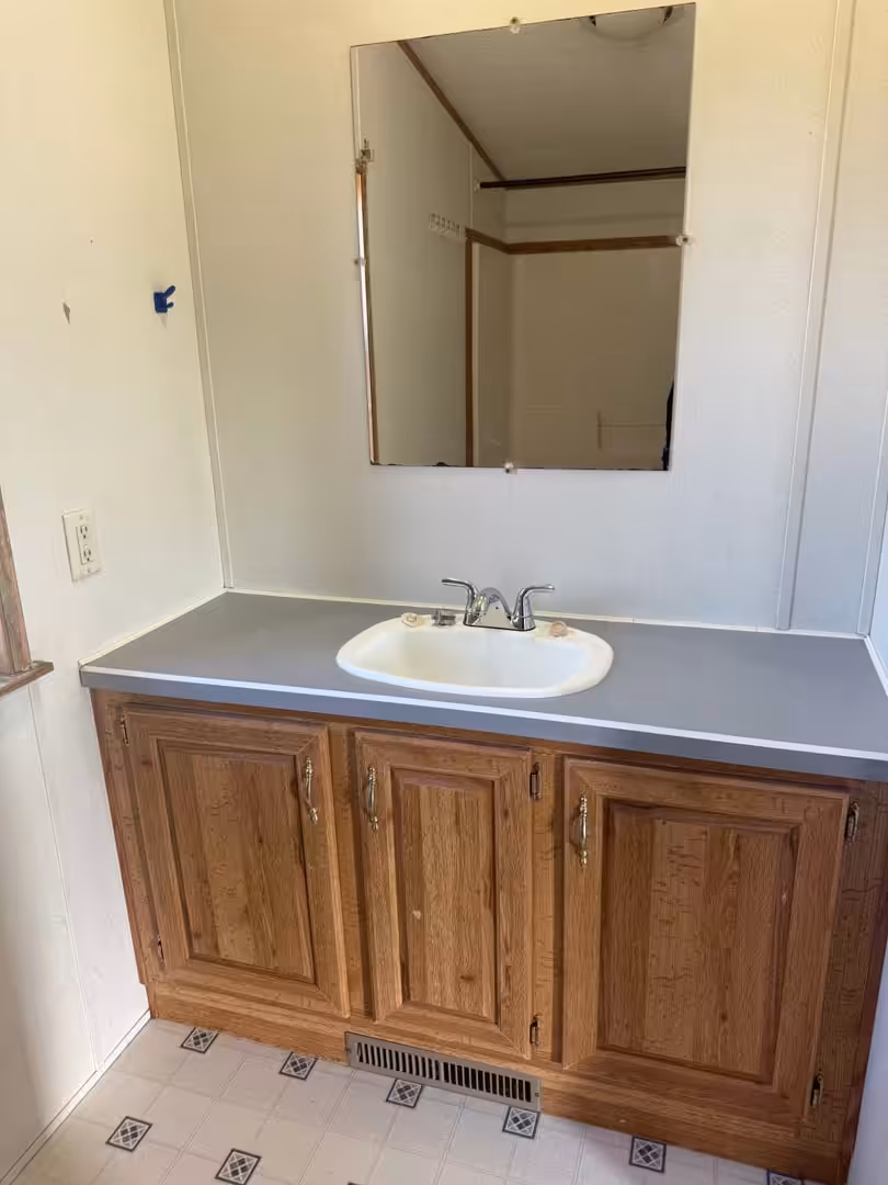 Bathroom vanity with oak cabinets, white sink, gray countertop, and wall mirror above.