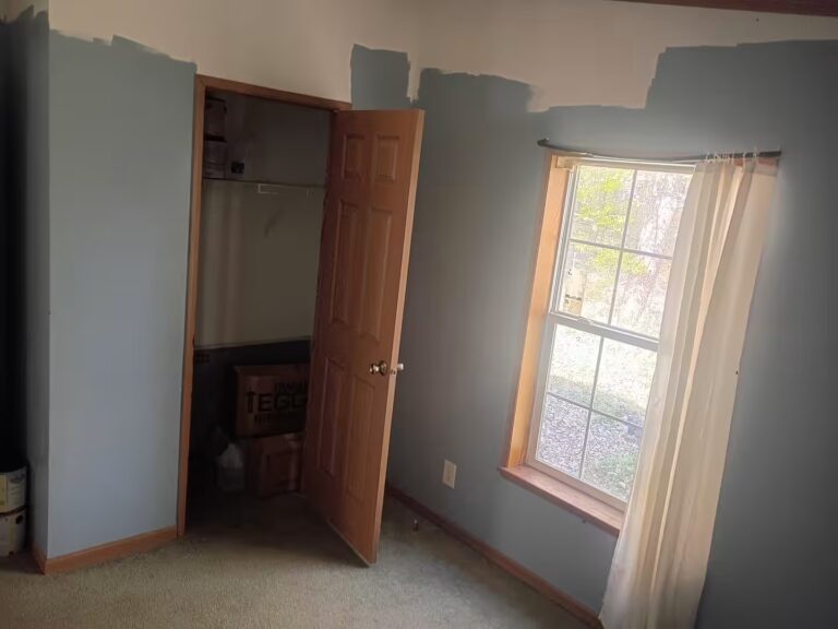 Room with partially painted blue walls, open closet door with TEGO box inside, and curtained window