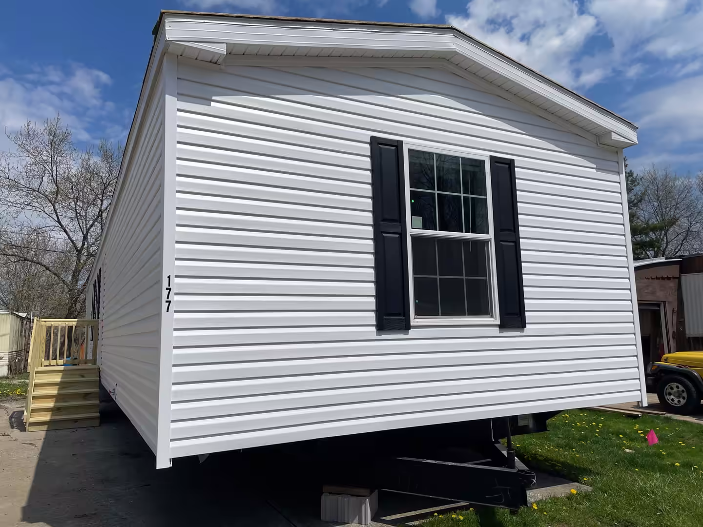White mobile home with black shutters marked 177, under a blue sky.