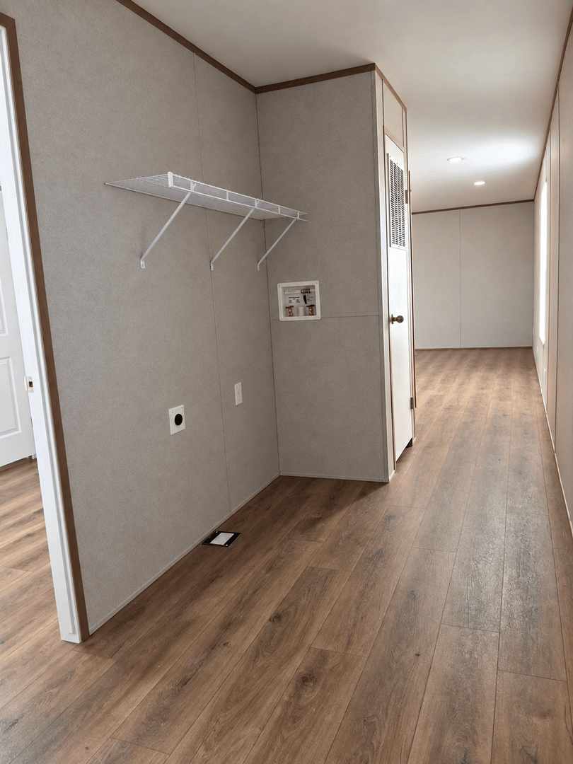 Empty room with wood-look flooring, white wire shelf on beige wall, and hallway with door