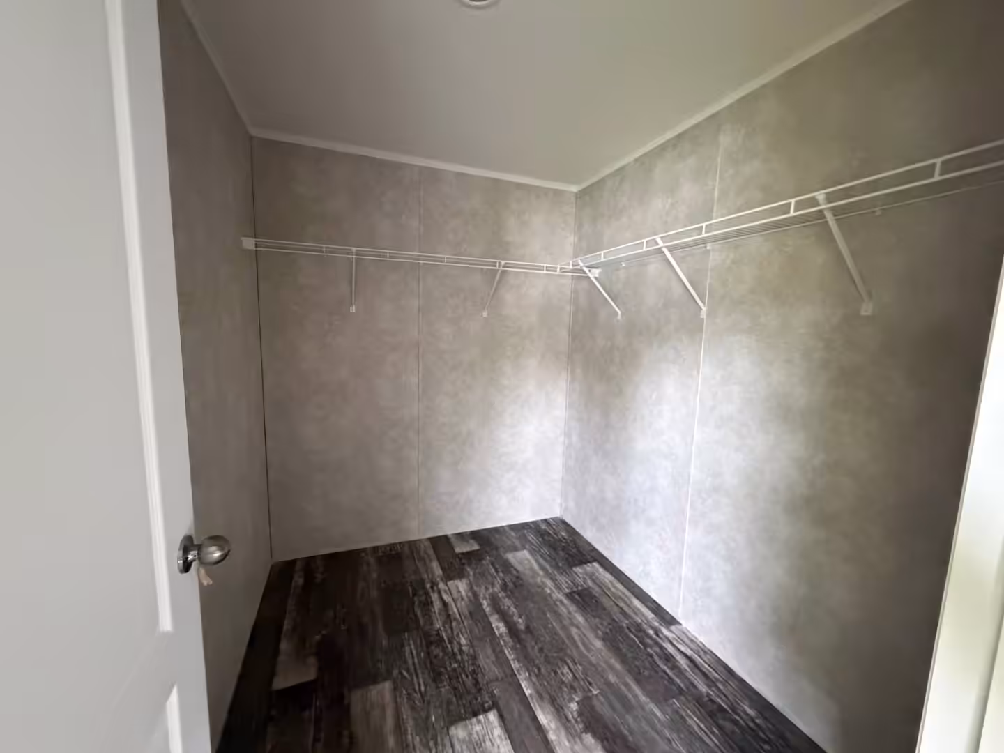 Empty walk-in closet with white wire shelving, gray walls, dark wood-look floor, and white door